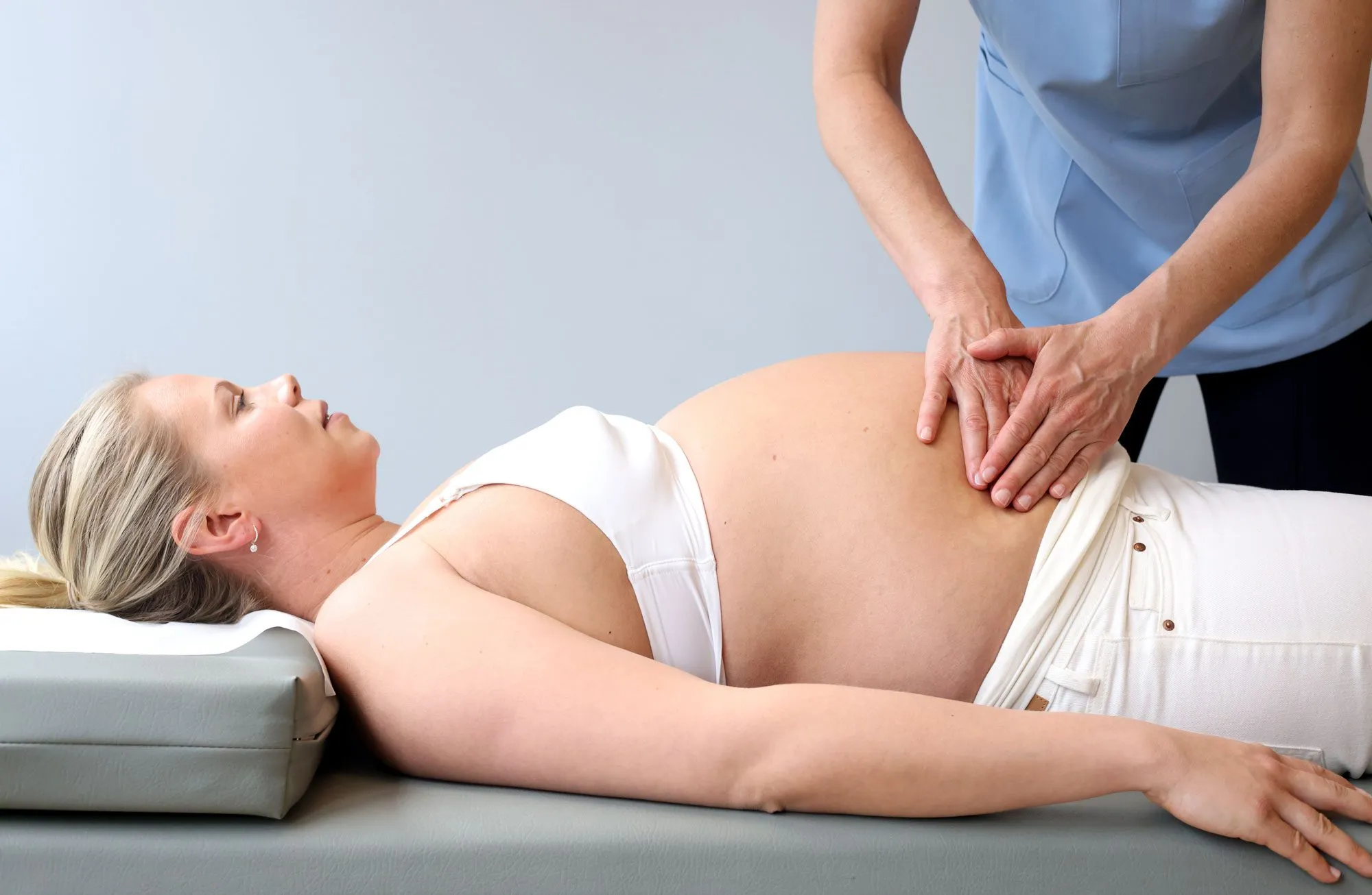 Kiropraktor jobber med de runde ligamentene hos en gravid kvinne som ligger på ryggen på behandlingsbenken