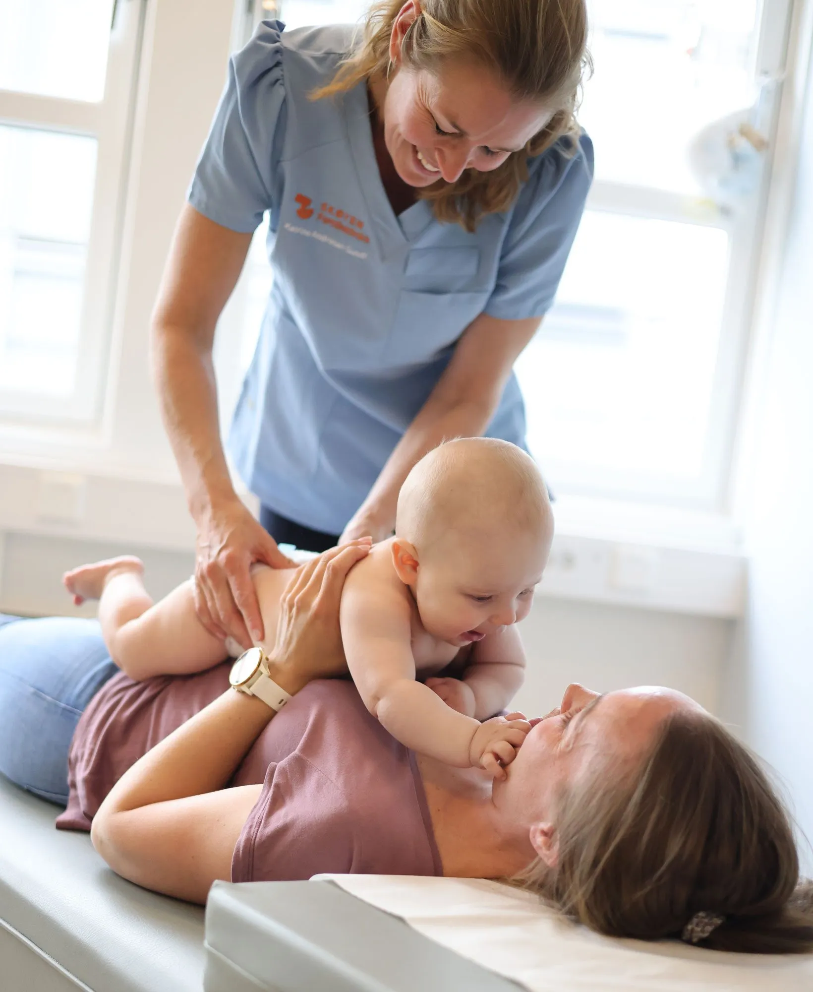 Kiropraktor Katrine Andresen Sundt behandler en smilende baby som ligger trygt på brystet til mor