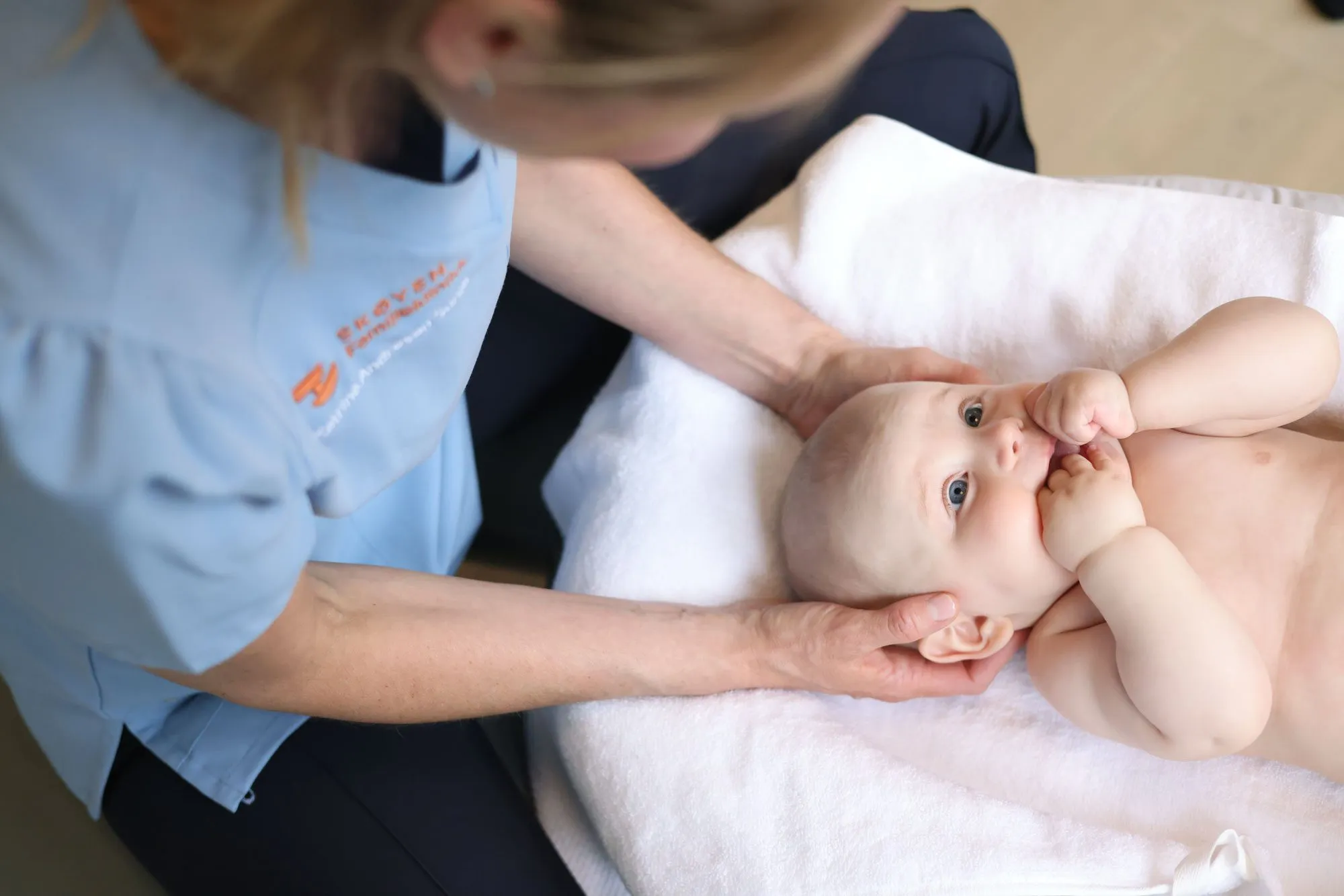 Kiropraktor holder forsiktig rundt hodet til en baby som ligger på ryggen